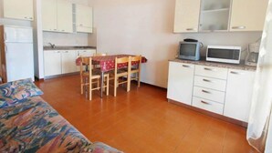Un ambiente compatto con angolo cottura, zona pranzo con tavolo e sedie, e divano.