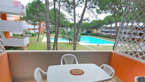 Un balcone con tavolo e sedie, vista su una piscina e vegetazione.