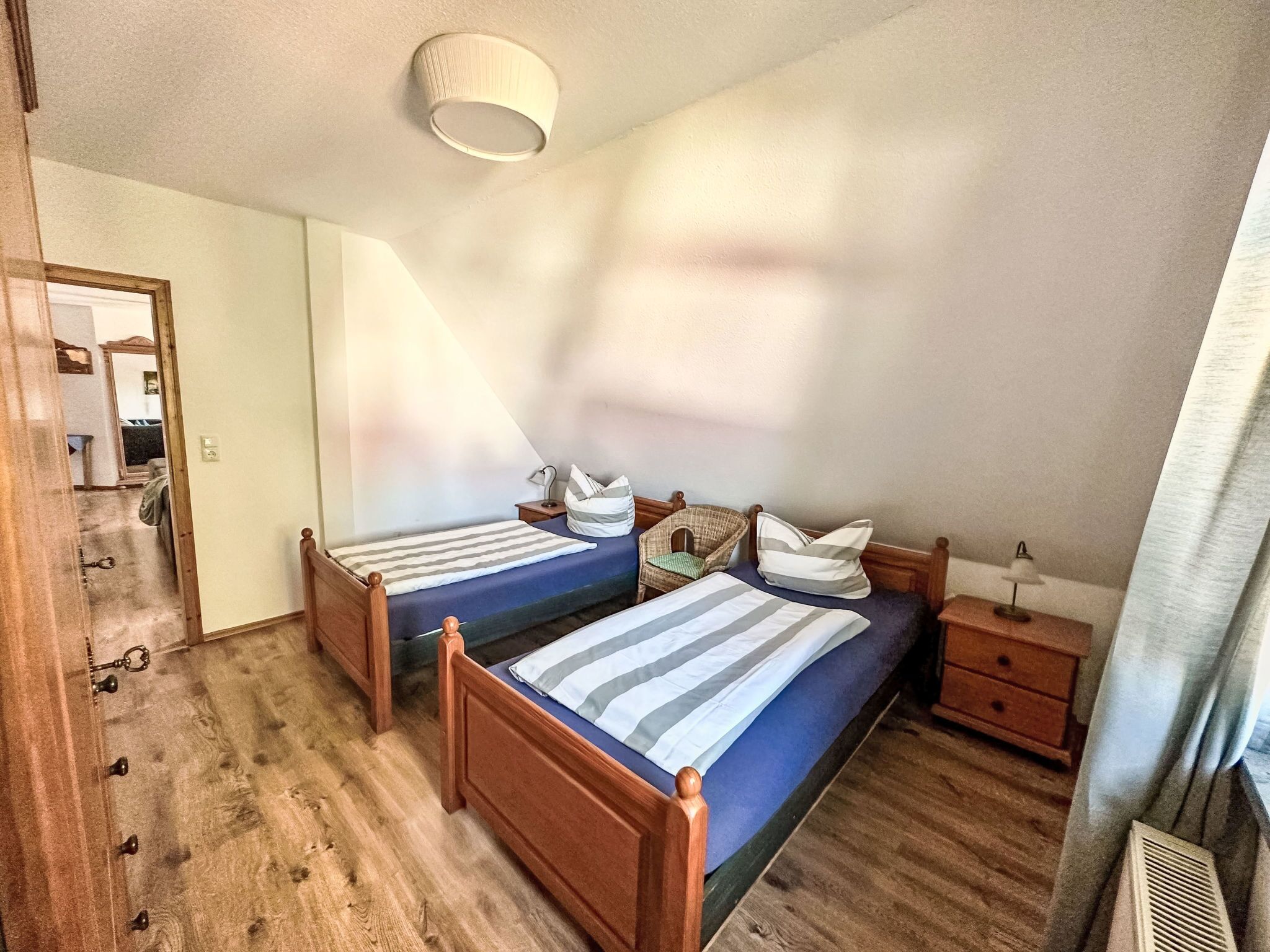 A bedroom with two wooden beds, a nightstand, a lamp, and a window with curtains.