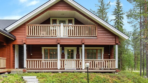 A two-story log cabin with a balcony, a porch, and a small front yard.