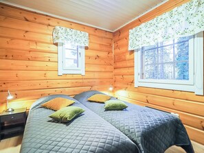 A wooden cabin room with two beds, a nightstand, a lamp, and a window with a view of trees. - Kiela 1 by Interhome (Kittilä)
