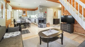 A cozy living room with a sofa, coffee table, and TV, connected to a kitchen with a dining area and a fireplace.