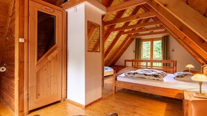 Une cabane en bois avec une chambre à coucher aménagée en mezzanine, un sauna et une grande fenêtre donnant sur un paysage verdoyant.