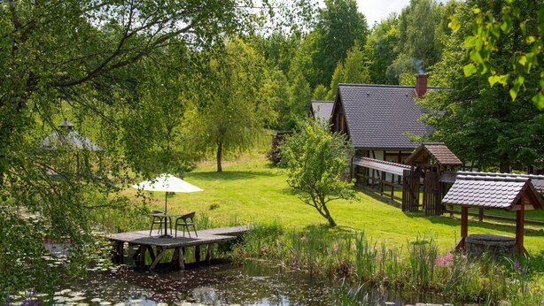 Un chalet au bord du lac, doté d’un quai, entouré d’une végétation luxuriante et bordé d’un étang où flottent des nénuphars.