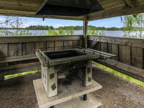 Un espace barbecue extérieur rustique, avec une table et des bancs en béton, entouré de rampes en bois, et offrant une vue sur un lac.