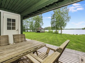 A wooden deck with a table and benches, overlooking a grassy area with a lake and trees.