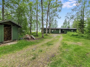 Une cabane verte avec une terrasse en bois et une pile de bois de chauffage.