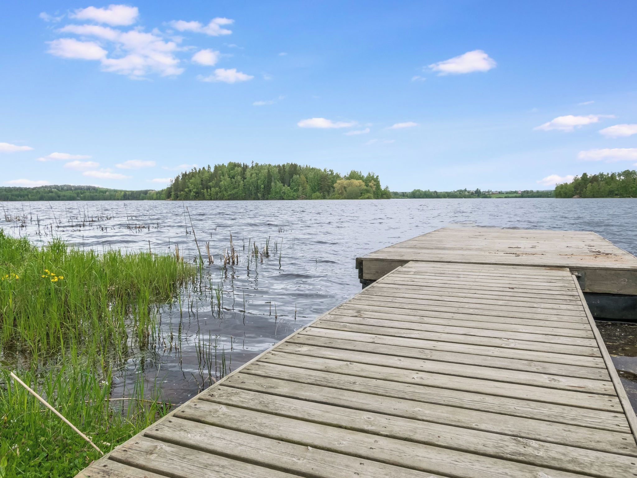 Une jetée en bois s’étendant sur un lac paisible, avec une île boisée visible au loin.