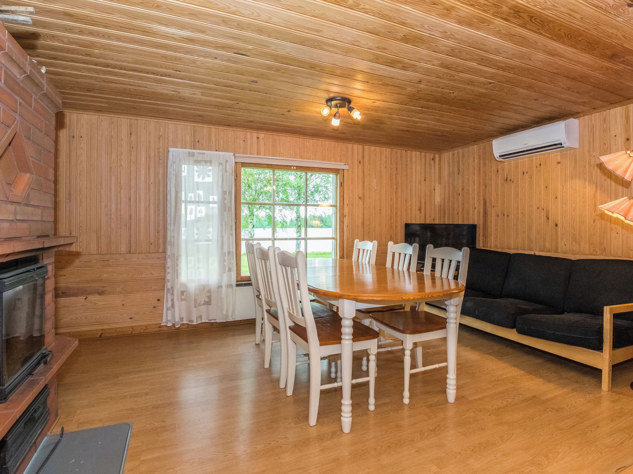 A wooden cabin interior with a dining table, chairs, a sofa, and a fireplace.