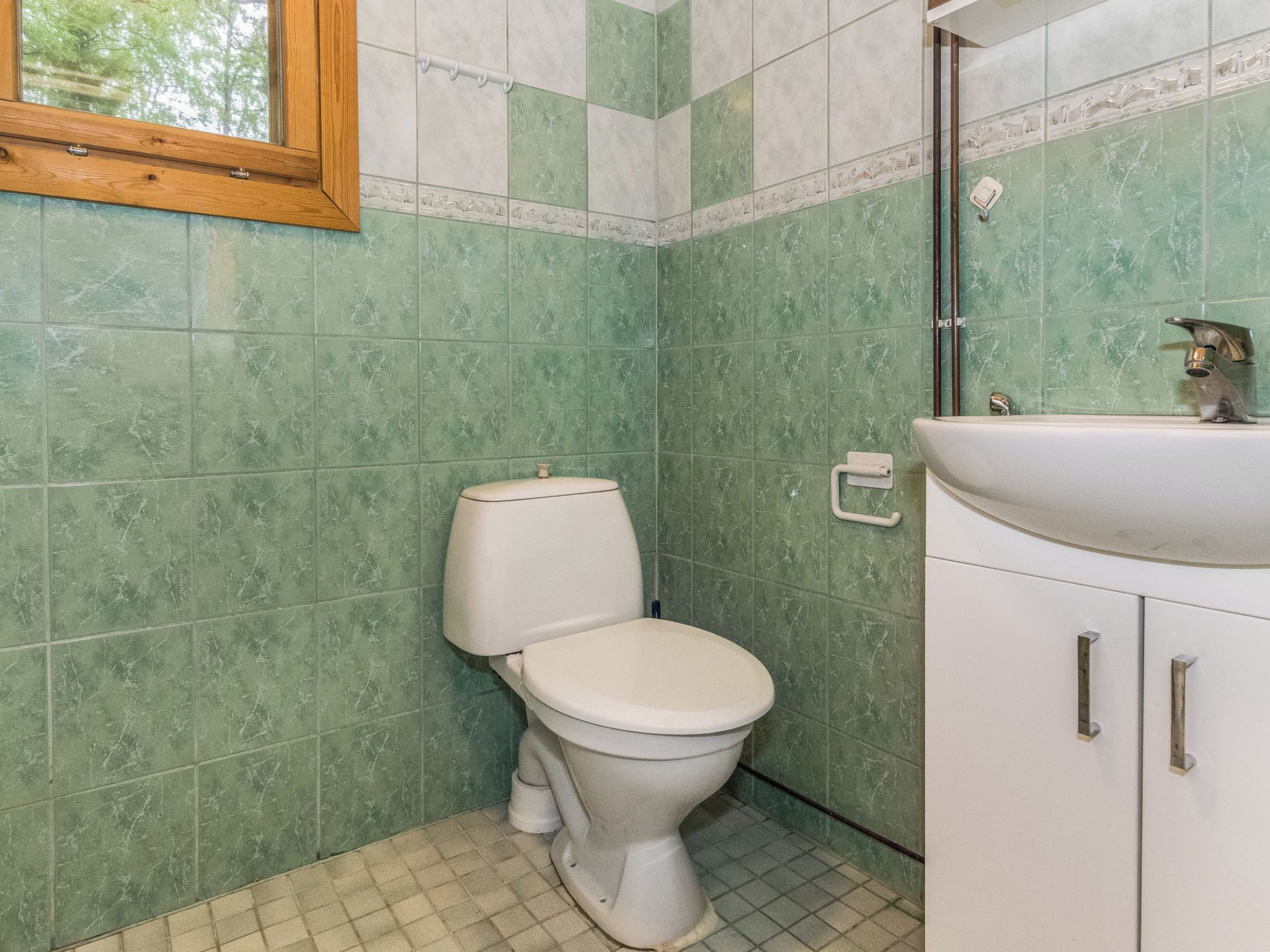 A bathroom with a toilet, sink, and cabinet.