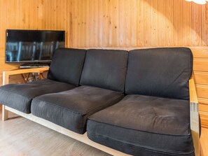 Un canapé noir avec une structure en bois et un téléviseur posé sur un meuble en bois.