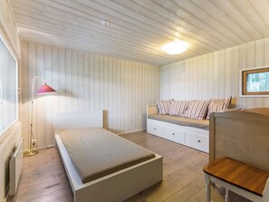 A room with a bed, a bench with cushions, a desk, and a lamp.
