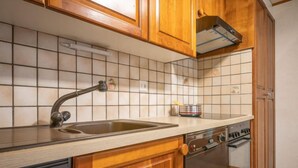 A kitchen with wooden cabinets, a stainless steel sink, a dishwasher, and a tiled backsplash. - Le Tzanton by Interhome (Ovronnaz)