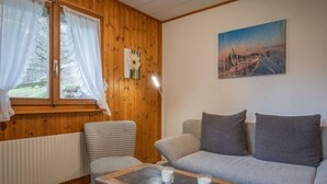 A cozy living room with a wooden paneled wall, a grey sofa, a patterned armchair, and a coffee table with candles. - Le Tzanton by Interhome (Ovronnaz)