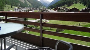 Un balcon donnant sur un village de montagne, avec une balustrade en bois et une table entourée de chaises.