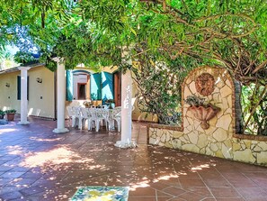 An outdoor patio area with a dining setup, stone walls, and a decorative lion head. - Orchidea by Interhome (Siracusa)