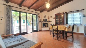 Een ruime woonkamer met een houten plafond, een eettafel met stoelen, een bank en een open haard.