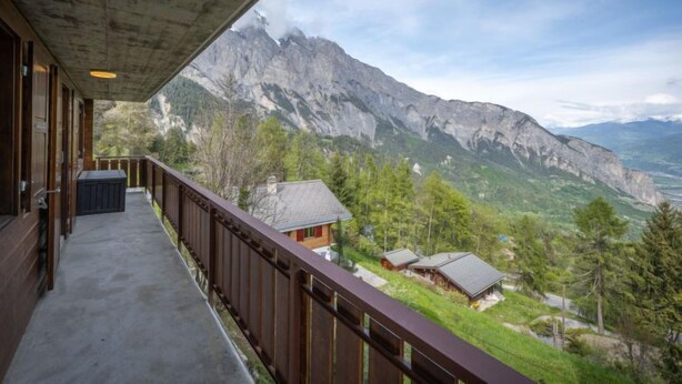 A balcony with a view of a mountain range and a small village below. - Falaises by Interhome (Ovronnaz)