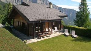 A chalet with a sloped roof, wooden exterior, and a patio with lounge chairs and a bench. It is surrounded by a well-maintained lawn and a mountain backdrop. - Falaises by Interhome (Ovronnaz)
