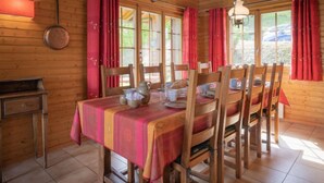 A wooden dining room with a table set for four, red curtains, and a hanging light fixture. - Falaises by Interhome (Ovronnaz)