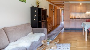 Ein Wohnzimmer mit einer Couch, einem Couchtisch und einem Teppich. Es gibt eine Küchenzeile mit Holzschränken und einem Esstisch.