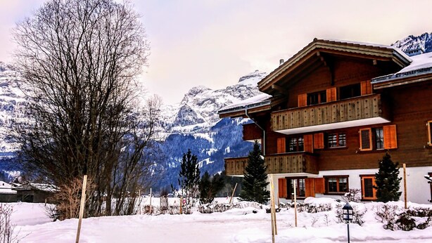 Ein mehrstöckiges Holzhaus mit Balkonen, umgeben von schneebedeckten Bergen und Bäumen.