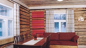 A cozy cabin interior with a wooden log wall, a dining table with chairs, a red sofa, and a window with curtains. - Eteläranta by Interhome (Hankasalmi)