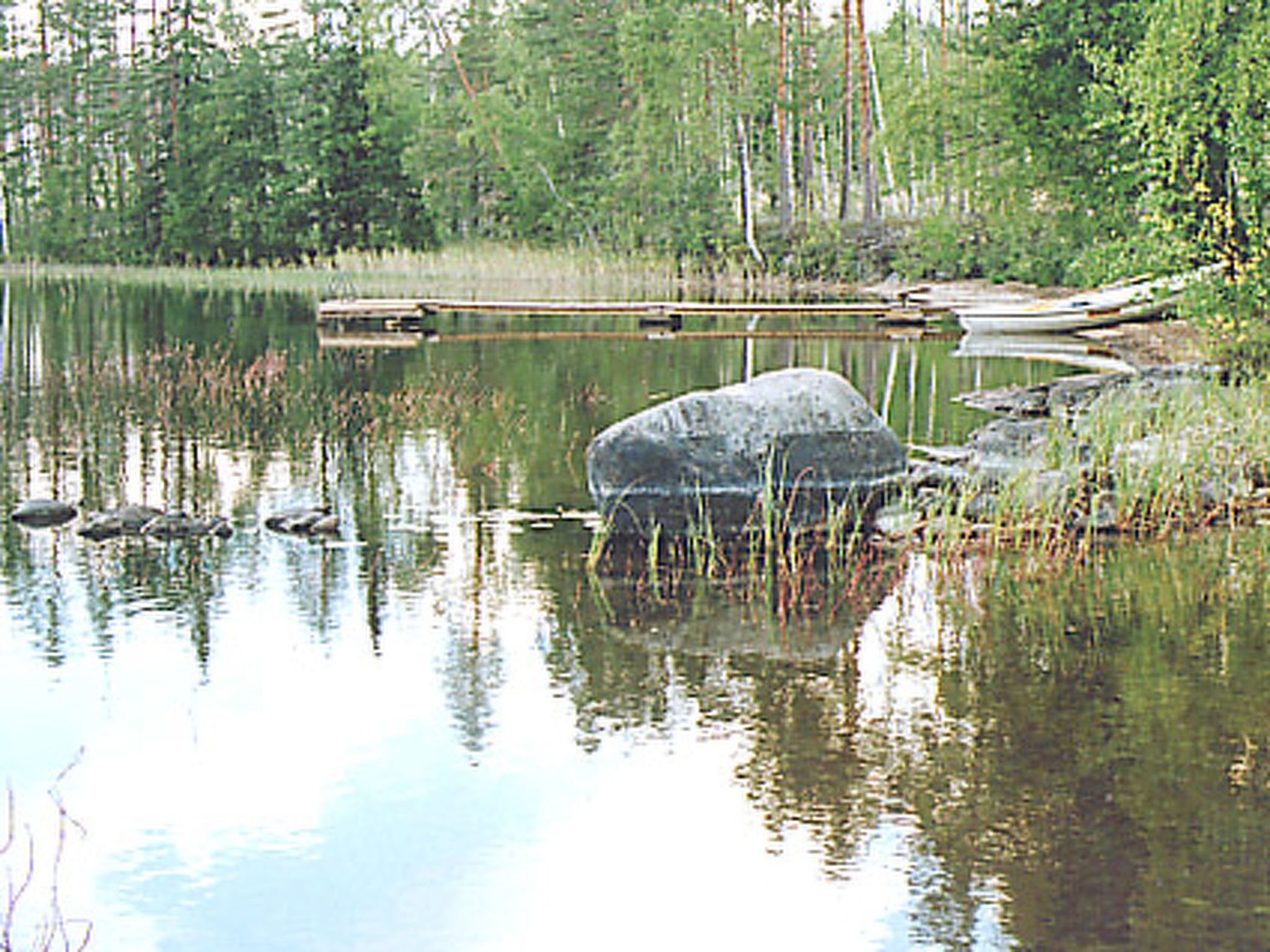 A calm lake with a large rock in the center, surrounded by trees and a dock.