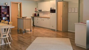 A modern kitchen with wooden cabinets, a dining area with a table and chairs, and a bookshelf. - Am Ryschbächli by Interhome (Zweisimmen)