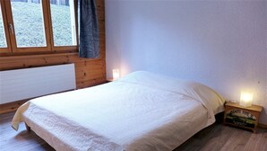 Makuuhuone, jossa on sänky, puuseinät, ikkuna ja yöpöytä, jossa on lamppu.