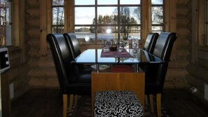 A dining area with a glass table, two black leather chairs, a chandelier, and a view of a snowy landscape through large windows.