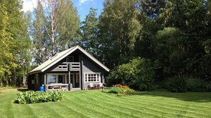 A lodge with a large porch, surrounded by a well-maintained lawn and dense trees.