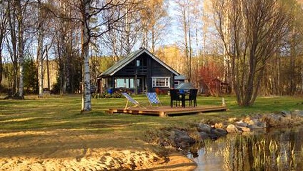 A cabin with a dock extending into a pond, surrounded by trees.