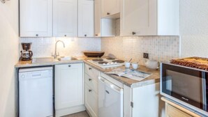 Cocina compacta con armarios blancos, horno empotrado, cafetera y microondas.