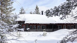 A cabin with a snow-covered roof, surrounded by trees and a wooden deck.