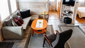 A cozy living room with a sofa, a small table, a chair, a television, and a painting on the wall.