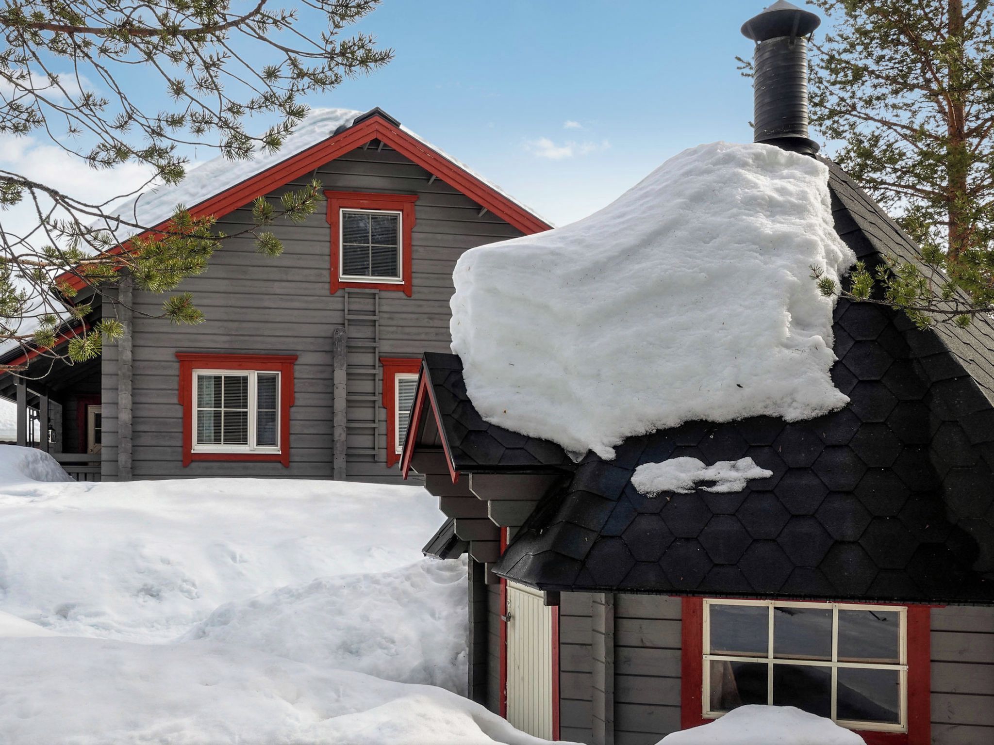 A two-story house with a red roof and a chimney covered in snow.