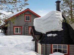 A two-story house with a red roof and a chimney covered in snow.