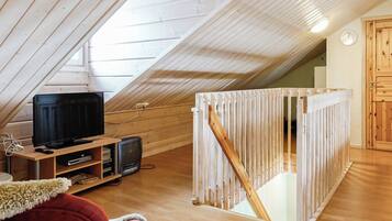 A room with a sloped ceiling, wooden flooring, a television, a small television, and a red chair.