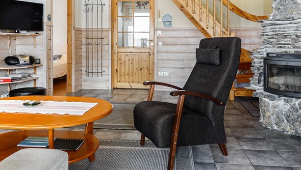 A cozy living room with a stone fireplace, wooden staircase, and a flat-screen TV.