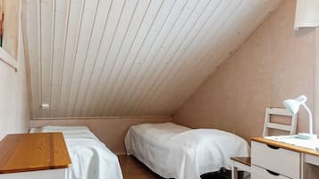 A small, single-room with two beds, a desk with a chair, and a lamp.