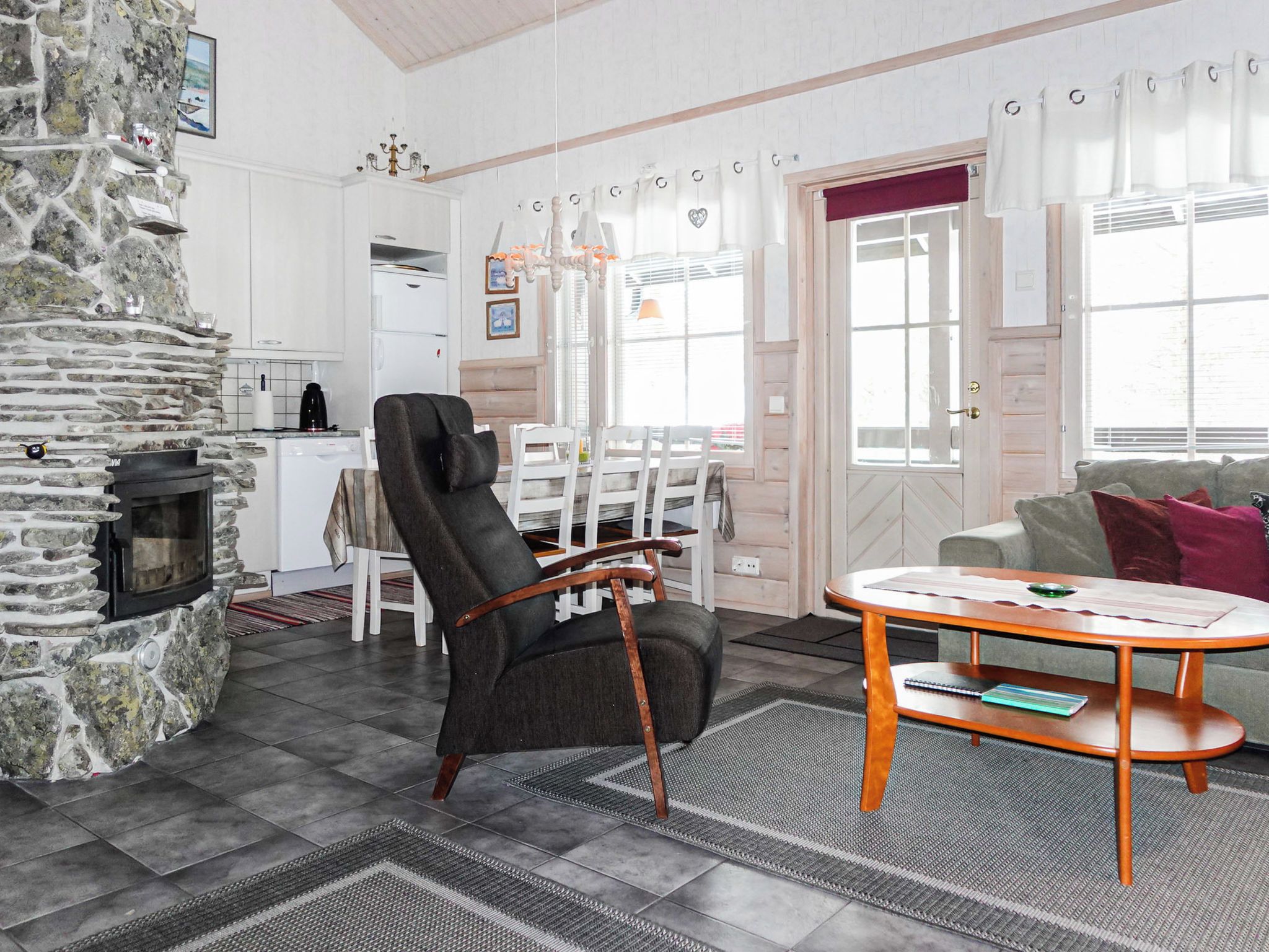 A cozy living room with a stone fireplace, a dining area with a table and chairs, and a sofa with cushions.