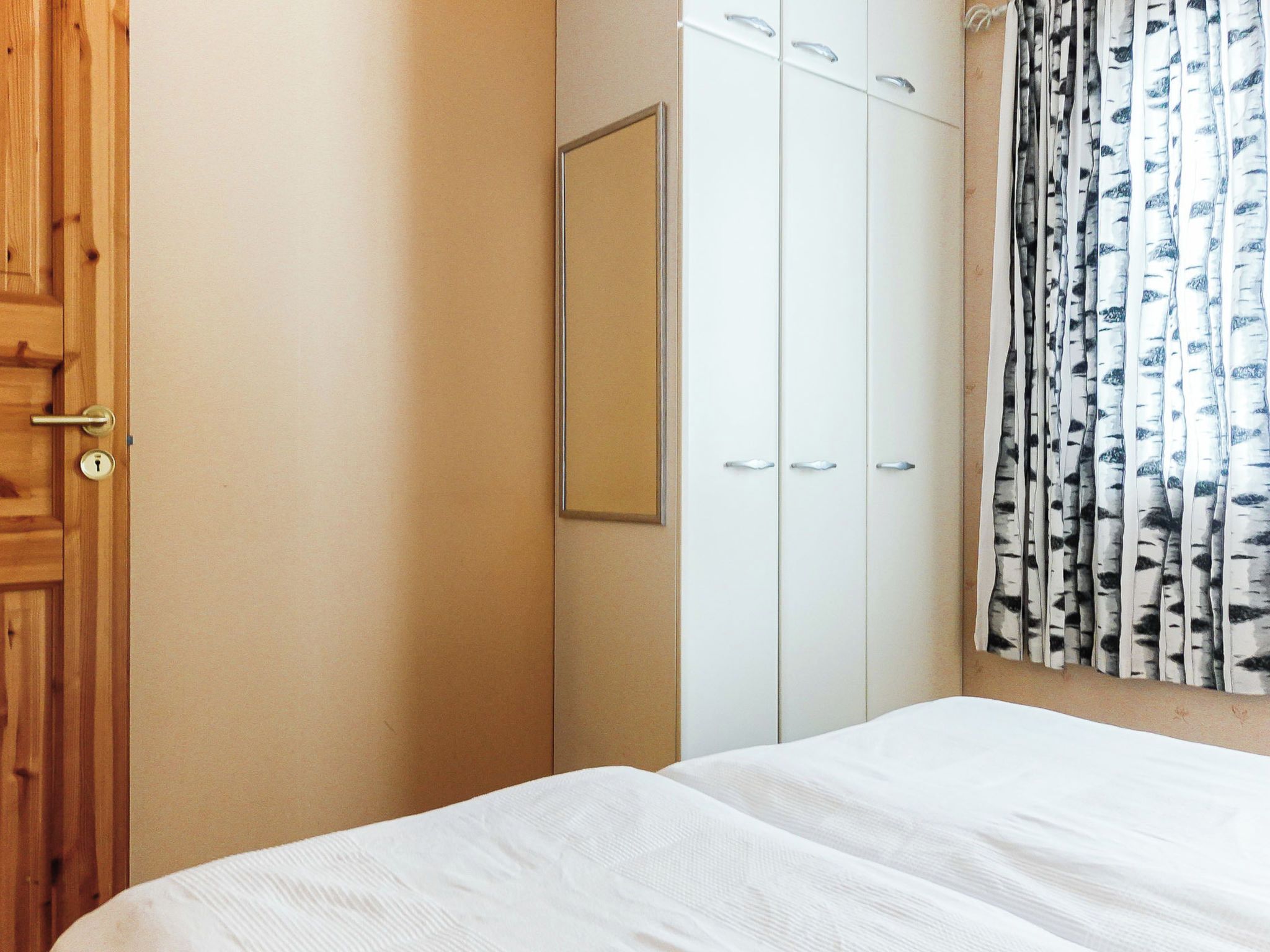 A bedroom with a wooden door, a wardrobe, and a bed with white bedding.