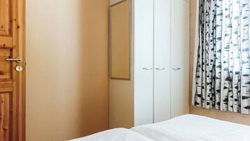 A bedroom with a wooden door, a wardrobe, and a bed with white bedding.