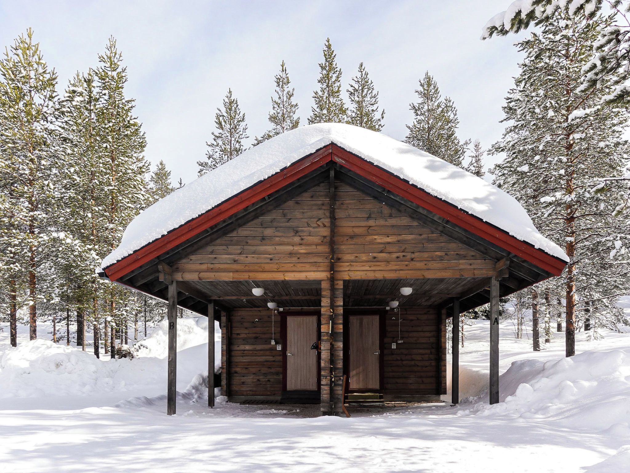 A wooden cabin with a snow-covered roof, surrounded by snow-covered trees.