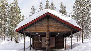 A wooden cabin with a snow-covered roof, surrounded by snow-covered trees.