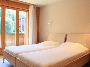 A room with two single beds, wooden walls, a balcony with a sliding door, and a view of greenery outside. - Ambassadeur 15 by Interhome (Villars)
