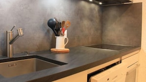 A modern kitchen with a stainless steel sink, a coffee cup holder with utensils, and a built-in dishwasher. - Ambassadeur 15 by Interhome (Villars)