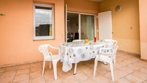 Un espace extérieur abrité, aménagé pour prendre les repas, avec une table et des chaises, une fenêtre et une porte-fenêtre coulissante.
