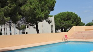 Une piscine à l’eau d’un bleu limpide, entourée d’un mur de couleur beige et d’arbres.